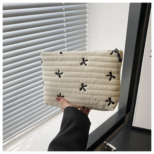 Detail of off-white quilted cosmetic pouch featuring black bow embroidery and zip closure