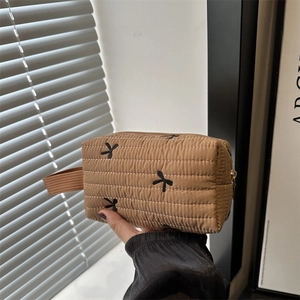 Quilted tan makeup bag with black bow embroidery and gold zipper held in hand