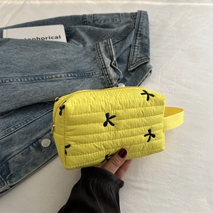 Quilted yellow makeup bag with embroidered black bows and a convenient side handle strap