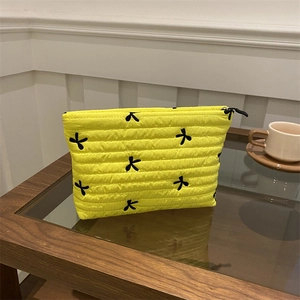 Chic yellow quilted cosmetic bag featuring black bow embroidery and secure zipper closure
