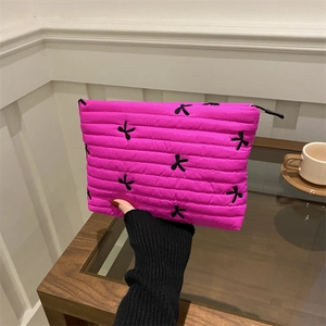 Pink quilted clutch with black bow embroidery and zip closure held in hand