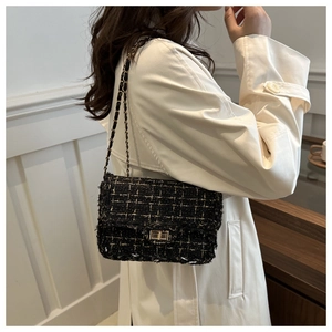 Close-up of black tweed fabric texture and gold chain strap on woman's crossbody bag