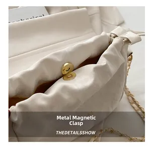 Detail shot of the secure gold magnetic clasp on a pleated cream chain bucket bag