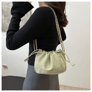 Detail of light green drawstring bucket bag with pleated texture and chain strap on shoulder