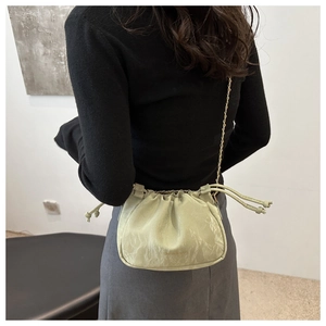 Detail of light green pleated crossbody bag with gold chain strap on model shoulder
