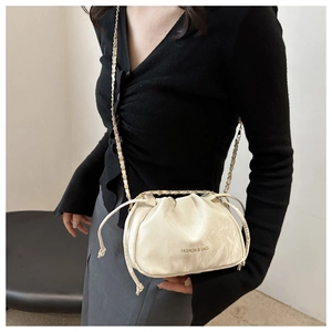 Detail of cream drawstring pleated cloud bag with elegant metal chain shoulder strap