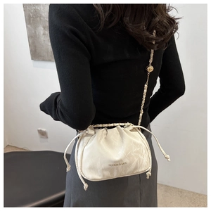 Close-up of cream drawstring bucket bag with chain strap and gold adjustment buckle