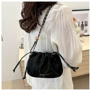 Detail of black drawstring bucket bag with gold ball chain strap and fashion text