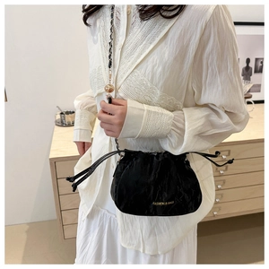 Detail of black leather drawstring bucket bag with gold chain strap and spherical charm