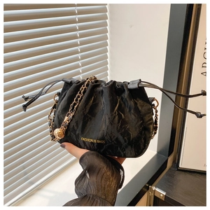 Detail of black pleated cloud bag featuring gold chain and decorative sphere charm