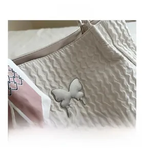 Détail du sac cabas blanc cassé avec texture ondulée, boucle papillon et foulard en soie