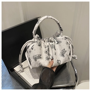 Detail of white pleated tote bag with black butterfly print held by a model