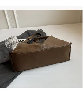 Detailed view of dark brown textured tote bag with gold buckle on grey blazer backdrop