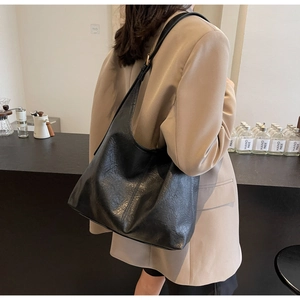 Chic black tote bag in crinkled faux leather texture shown in a cafe setting
