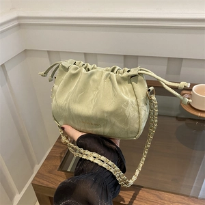 Light green pleated drawstring bucket bag with gold chain strap shown in hand