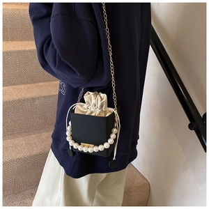 Close-up of black bucket bag with large pearl handle and gold chain on stairs