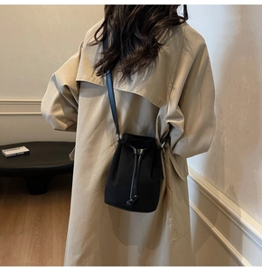Side view of a black drawstring bucket bag worn over a khaki trench coat