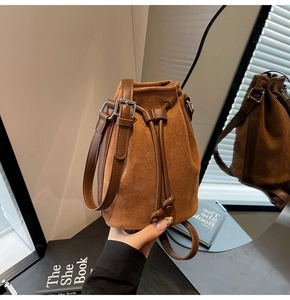 Detail of brown faux suede bucket bag featuring drawstring closure and leather strap