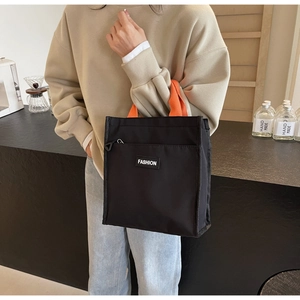 Détail du sac cabas en toile noire avec poignées orange et étiquette mode pour femmes