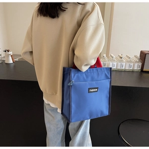 Detail of blue tote bag featuring red handles and a Fashion woven label on the front