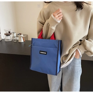 Détail du sac cabas en toile bleue avec anses rouges et étiquette Fashion au café