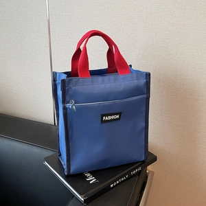 Blue and red contrast nylon tote bag with black Fashion label on a book background