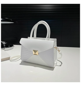 Detail of white crocodile embossed texture on a sleek square handbag with gold stud