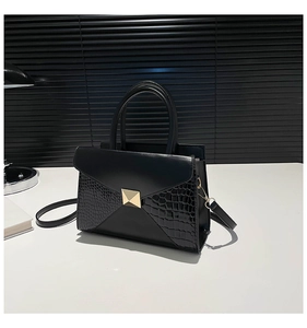 Detail of black faux leather bag with crocodile texture and gold square rivet clasp