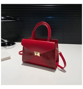 Detail of red crocodile texture handbag with golden triangle buckle on white table
