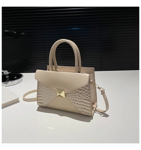 Detail of beige crocodile textured crossbody bag with gold buckle and accordion sides