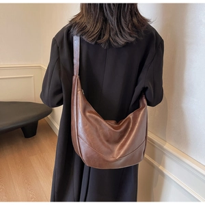 Close-up of a large dark brown faux leather hobo bag styled with a black coat