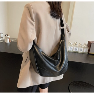 Detail of a large black crescent crossbody bag made of shiny soft PU leather with strap