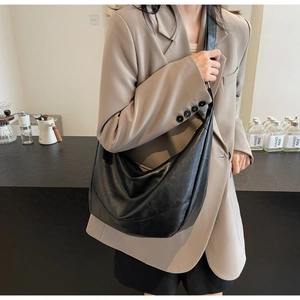 Detail of a large black crescent crossbody bag with textured faux leather and pleats
