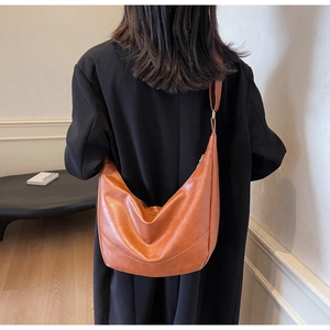 Brown faux leather crescent tote bag worn by a model in a modern interior setting