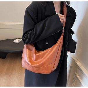 Model wearing a caramel leather hobo bag featuring a pebble texture and wide strap