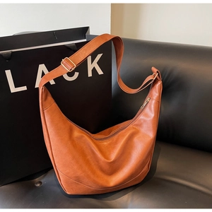 Detailed shot of caramel brown faux leather dumpling bag on black sofa