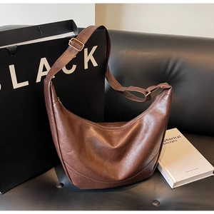 Detail of a dark brown vintage hobo bag with adjustable strap on a leather sofa