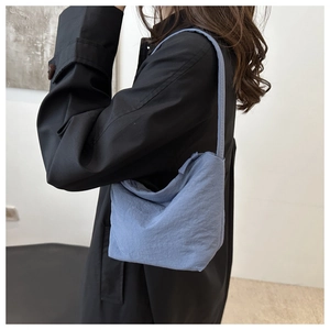 Sac seau bleu clair style bohème porté sous le bras avec un manteau noir élégant