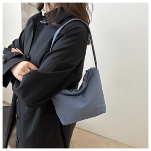Detail view of blue canvas shoulder bag featuring elegant pleated fabric and curved design