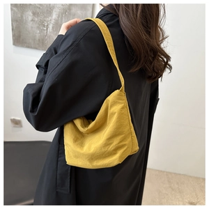 Détail d'un sac bandoulière en toile jaune gingembre porté sur un manteau noir élégant