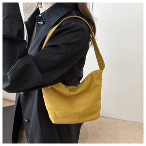 Détail d'un sac sous le bras en toile jaune vif avec une bandoulière large sur tenue noire