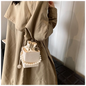 Detail of white bucket bag with pearl handle, geometric texture, and golden chain strap
