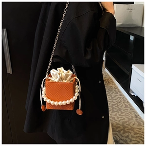 Detail of orange woven bucket bag with large pearl handle and golden chain strap
