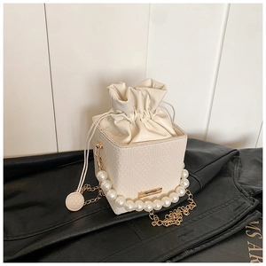 Close-up of pearl handle and woven texture on a cream bucket bag with drawstring