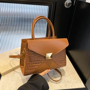Brown crocodile embossed leather crossbody handbag with gold buckle in warm studio setting