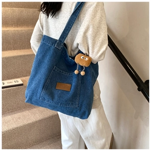 Detail der blauen Jeans-Tasche mit Leder-Logo und braunem Plüschbären-Anhänger