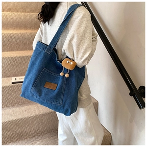 Detail der blauen Denim-Einkaufstasche mit Lederetikett und gelbem Plüsch-Anhängsel