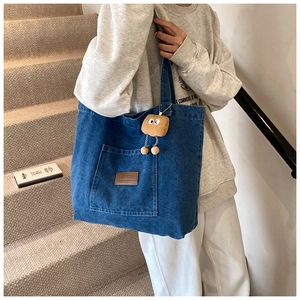Detail der blauen Denim-Einkaufstasche mit Lederlogo und flauschigem Toast-Anhänger