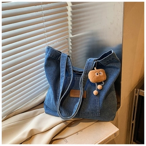 Detail der blauen Denim-Tragetasche mit Fronttasche, Lederetikett und Plüschbär-Anhänger