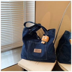 Detail der dunkelblauen Denim-Tragetasche mit Leder-Markenlabel und Plüsch-Toast-Anhänger